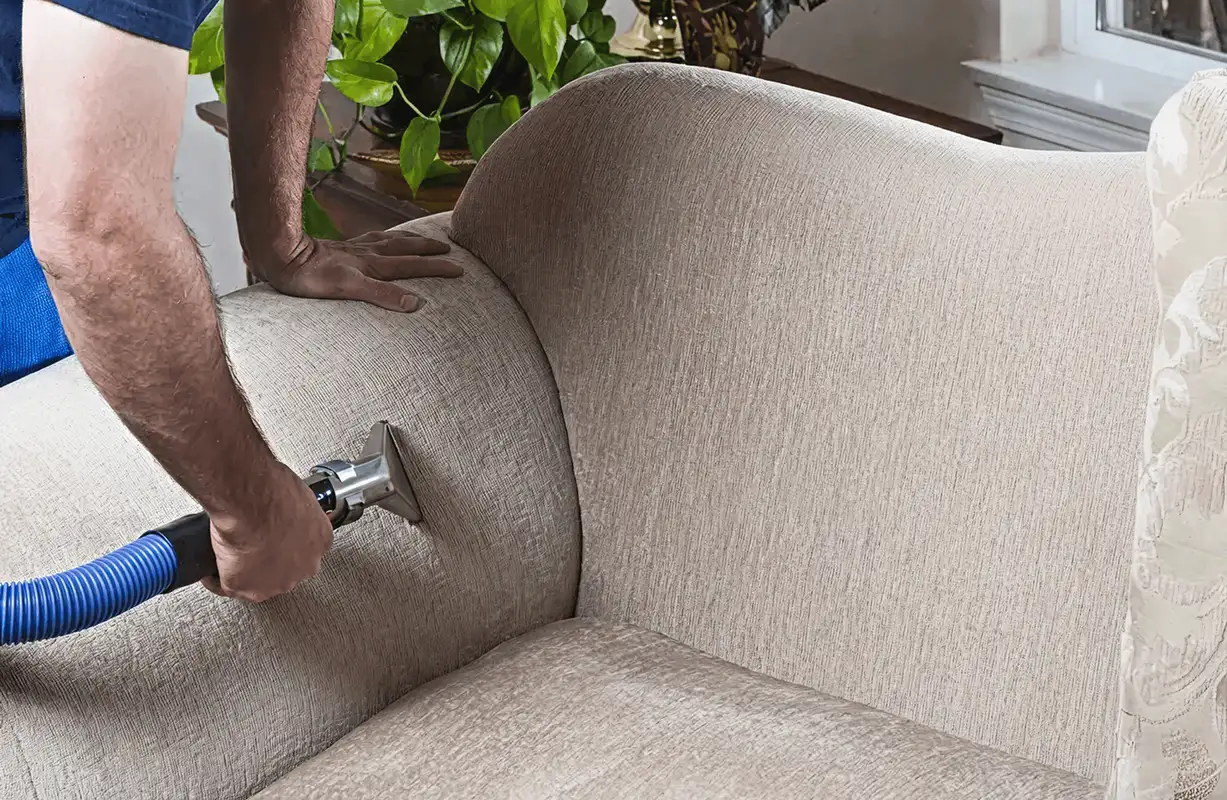 Professional upholstery cleaner deep-cleaning a fabric sofa with a handheld extraction tool and hose, Memphis, TN.